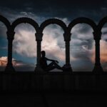 silhouette photo of person leaning on arch pillar