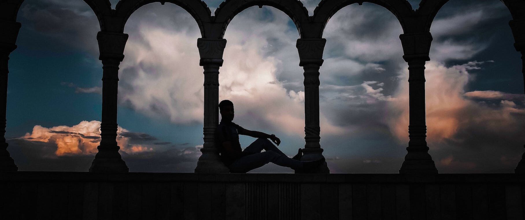 silhouette photo of person leaning on arch pillar