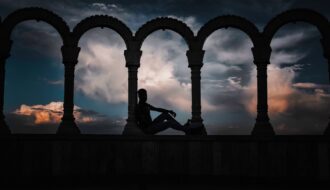 silhouette photo of person leaning on arch pillar