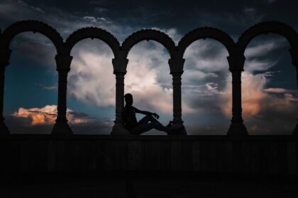 silhouette photo of person leaning on arch pillar