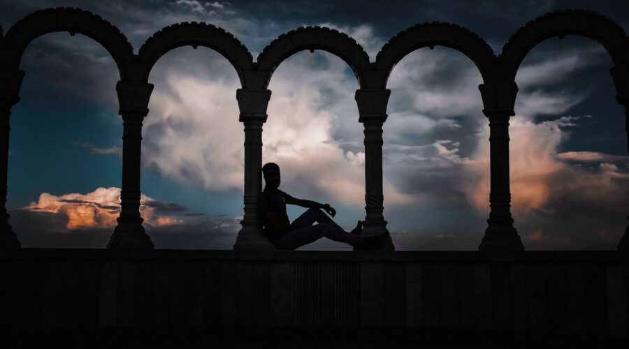 silhouette photo of person leaning on arch pillar